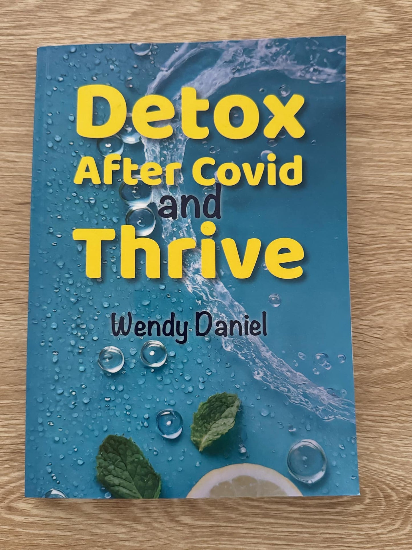 Book cover of 'Detox After Covid and Thrive' by Wendy Daniel – wellness guide with mint leaves, lemon slice, and water splash on blue background for post-COVID recovery and detox support