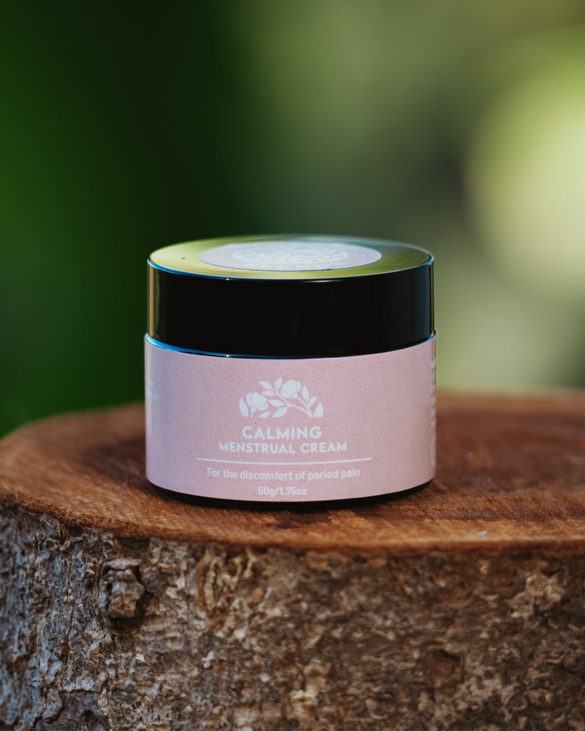 Calming Menstrual Cream 50g jar – natural topical relief for menstrual discomfort and period pain, displayed on a rustic tree stump with soft nature background